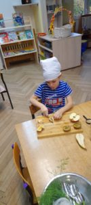 Chłopiec siedzi przy stoliku w chustce na głowie i kroi owoce 