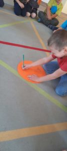Chłopiec ołówkiem rysuje na pomarańczowym kole z papieru 