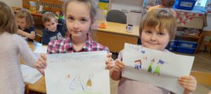 dziewczynka i chłopiec trzymają w dłoniach kartki z wykonanymi ilustracjami 