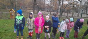Dzieci stoją w ogrodzie przedszkolnym trzymając w dłoniach latarenki 