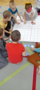 Dzieci siedzą na dywanie, przed nimi mata do kodowania