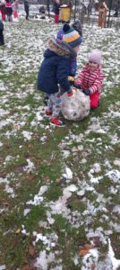 Dwoje dzieci toczy kulę śniegową w ogrodzie przedszkolnym 