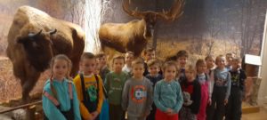 Dzieci stoją na tle eksponatów muzealnych - żubra i łosia 
