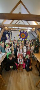 Dzieci na tle dekoracji Bożonarodzeniowych, trzymają w dłoniach papierowe choinki wykonane podczas warsztatów 