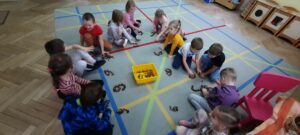 Dzieci siedzą na dywanie i układają cyfrę 6 z kasztanów 