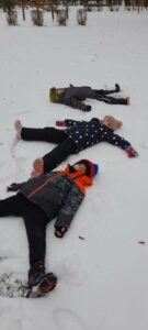 Troje dzieci robi na śniegu aniołki 