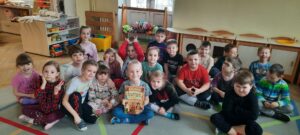20 dzieci siedzi na dywanie, jeden chłopiec trzyma książkę pt. "ilustrowane dzieje Polski" 