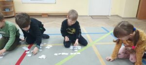 Czworo dzieci siedzi na dywanie i układa rytmy z obrazków znajdujących się na kwadratowych karteczkach 