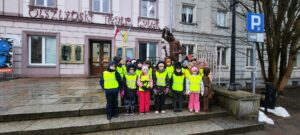 Przed budynkiem Olsztyńskiego Teatru Lalek stoi 17 dzieci w kamizelkach odblaskowych 