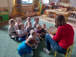 Przed gromadką dziesięciorga dzieci siedzi na krzesełku nauczyciel i czyta książkę pt. "Przygody Fenka. Myję ręce"