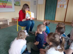 Nauczyciel pokazuje dzieciom siedzącym przed nim obrazki z czytanej książeczki