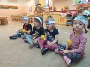 Dzieci z opaskami przedstawiającymi ziembę grają na grzechotkach