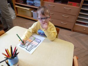 Chłopiec siedzi przy stoliku i koloruje obrazek