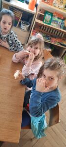 Trzy dziewczynki siedzą przy stoliku, w dłoniach trzymają kromki chleba 