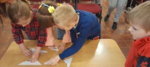 Troje dzieci układa puzzle z pociętej kartki. Jedno dziecko stoi obok i obserwuje. 