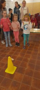 Trzy dziewczynki trzymają obręcze. Przed nimi stoi żółty pachołek. 