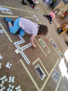 Dziewczynka układa puzzle na dywanie z trasą dla robota.