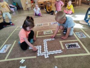 Dziewczynka i chłopiec układają puzzle na dywanie z trasą dla Ozobota.