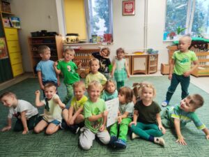 Grupa dzieci ubrana na zielono. Dwóch chłopców trzyma przepis na ogórki kiszone.