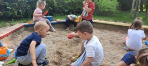 Na pierwszym planie dwóch chłopców naprzeciwko siebie, w tle dzieci bawiace się w piaskownicy. 