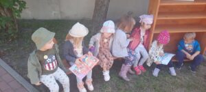 Kilkoro dzieci siedzi na ławce i ogląda książkę 