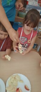 Dwoje dzieci nakłada kawałki owoców na drewniane patyczki do szaszłyków 