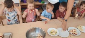 Kilkoro dzieci siedzi przy stoliku jedząc owocowe szaszłyki 