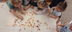 Dzieci przyklejają kolorowe liście na kartkę papieru 