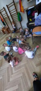 Grupa dzieci siedzi na podłodze przed pianinem 