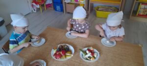Troje dzieci kroi na talerzykach owoce sezonowe: jabłka, gruszki i śliwki.