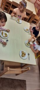 Kilkoro dzieci siedząc przy stoliku je owocowa sałatkę 