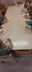 Kilkoro dzieci siedzi przy stoliku jedząc sałatkę owocowa 