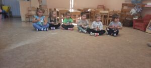 Grupa dzieci siedzi na dywanie, w dłoniach trzymają klawesy 