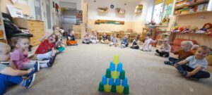 Dzieci siedzą na dywanie, na środku dywanu znajduje się wieża z kolorowych kubeczków. 