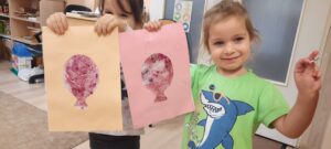Dwie dziewczynki trzymają w dłoniach kolorowe baloniki papierowe