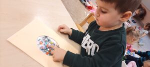 Chłopiec siedzi przy stoliku, palcem naciska kolorowe elementy znajdujące się na kartce 