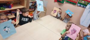 Kilkoro dzieci siedzi przy stoliku, w dłoniach trzymają kolorowe baloniki papierowe