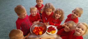 Grupa dzieci ubrana na czerwono. Na stoliku dwie miski z różnego rodzaju pomidorami.