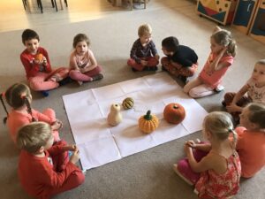 Grupa dzieci ubrana na pomarańczowo. Na dywanie różne rodzaje dyni.