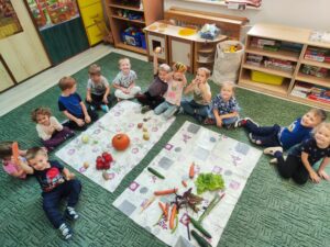 Grupa przedszkolaków przy matach z warzywami.