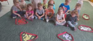 Dzieci siedzące na dywanie, na podłodze leżą szarfy w których są papierowe rybki (zbiory). Zabawy matematyczne.