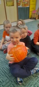 Chłopiec trzymający dużą, pomarańczową dynię .