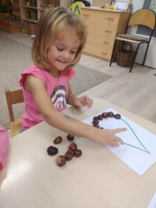 Dziewczynka układa rysunek z kasztanów