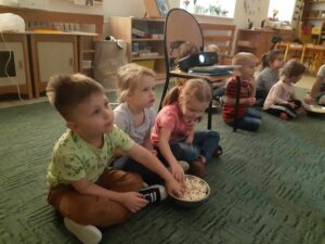 Dzieci siedzące na dywanie zajadające popcorn.
