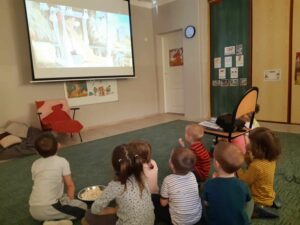 Grupa dzieci oglądające bajkę Kubusia puchatka na dużym ekranie.