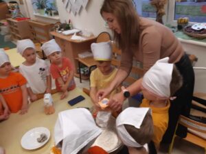 Nauczycielka razem z dziećmi przygotowująca ciasto na chleb.