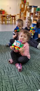 Troje dzieci prezentuje zbudowane przez siebie domy z klocków Lego.
