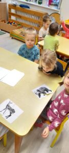 Dzieci siedzące przy stoliku układają puzzle z obrazem zwierząt leśnych.
