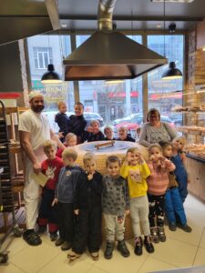 Grupa dzieci wraz z 2 nauczycielkami i piekarzem przy piecu