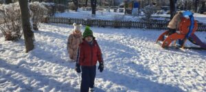 Dwoje dzieci stoi na trawniku, na którym jest śnieg 